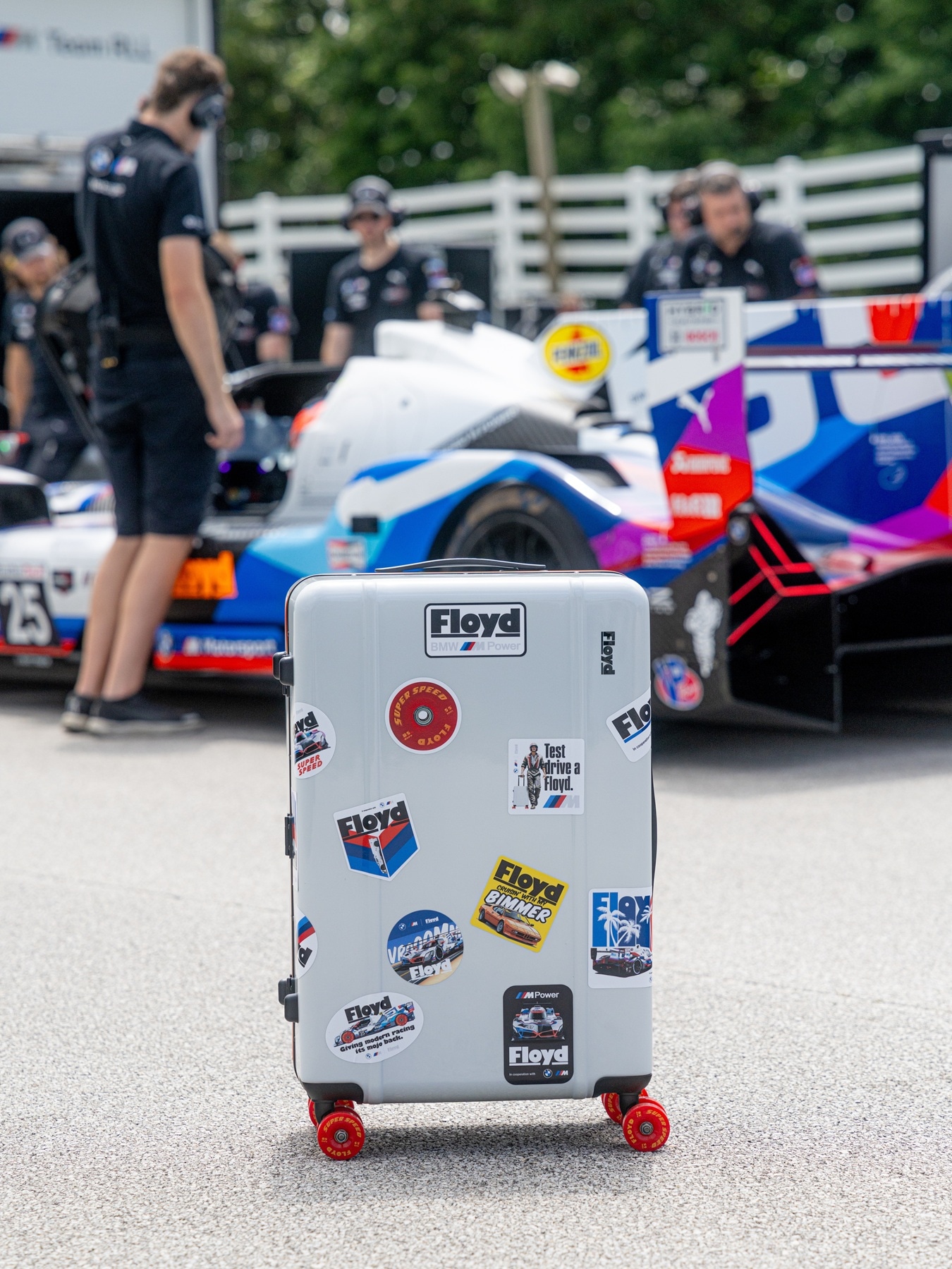 Floyd-Rollkoffer steht vor Rennfahrzeug BMW M Hybrid V8