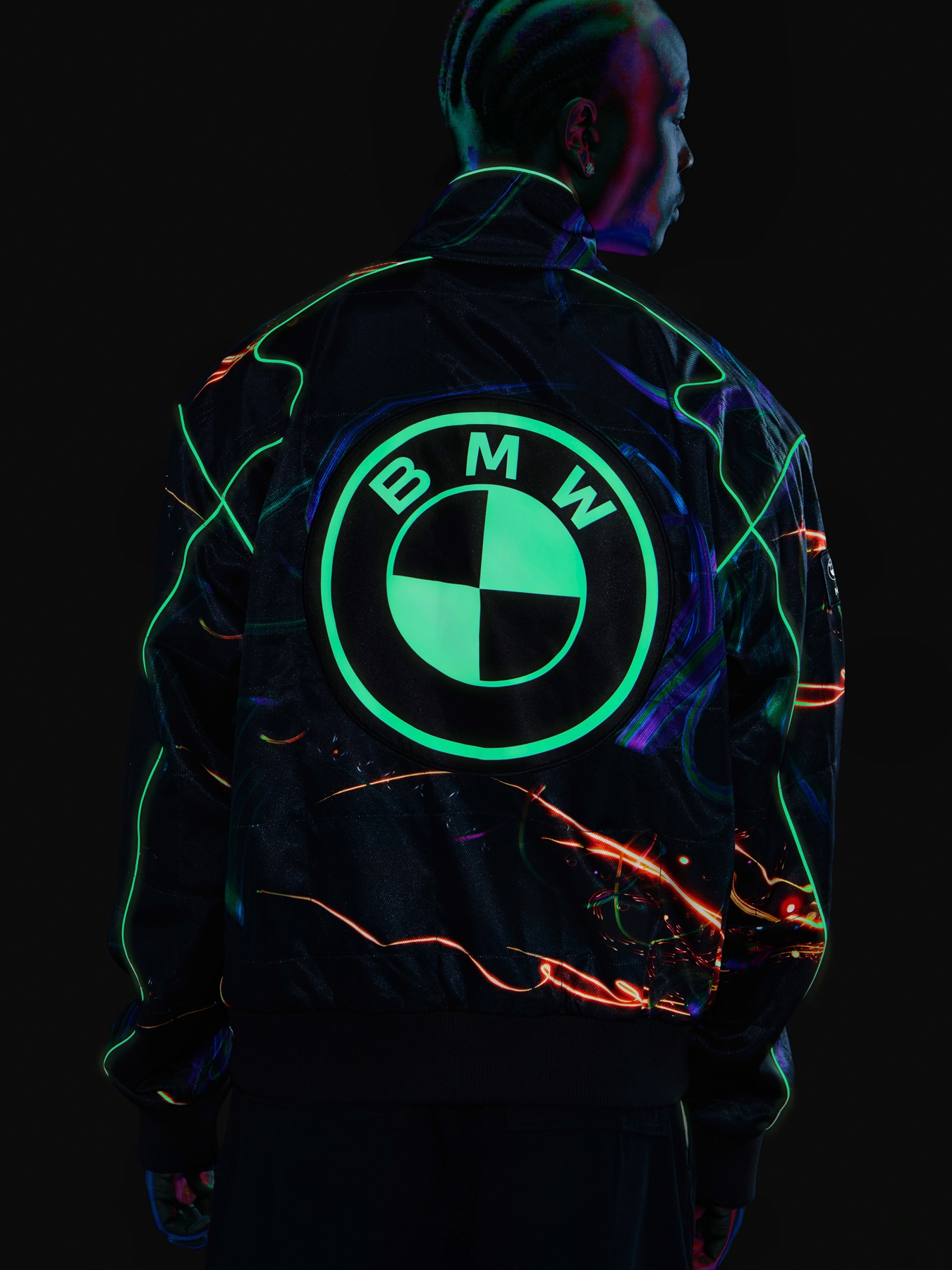 Junger Mann in Racer Jacke, auf der im Dunkeln ein BMW Logo leuchtet.
