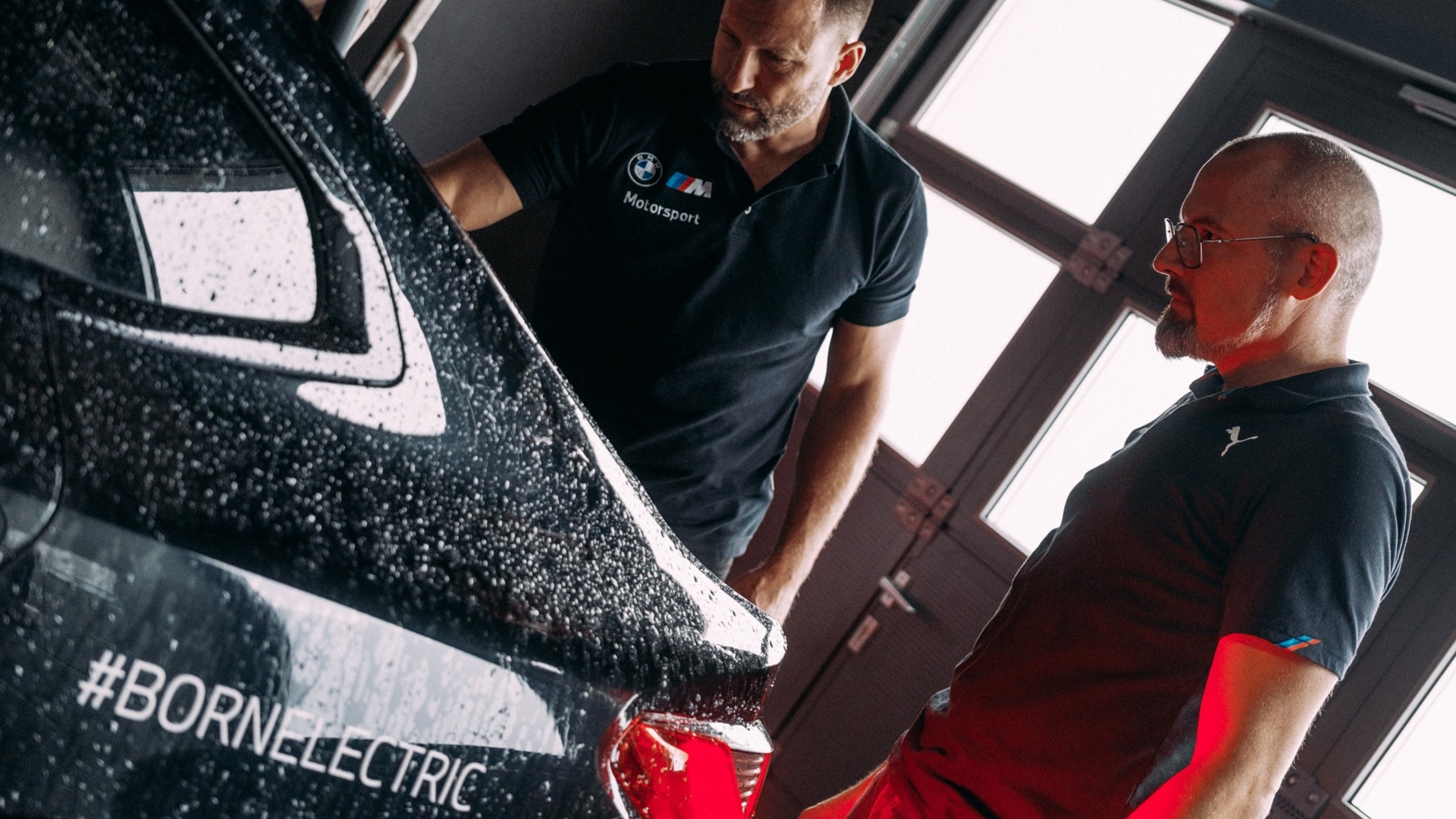 Zwei Ingenieure von BMW M beraten sich in einer Werkstatt für die Entwicklung von BMW M Elektrofahrzeugen.